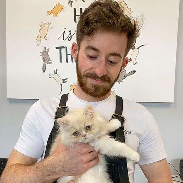 Man holding a fluffy white and tan kitten, smiling.