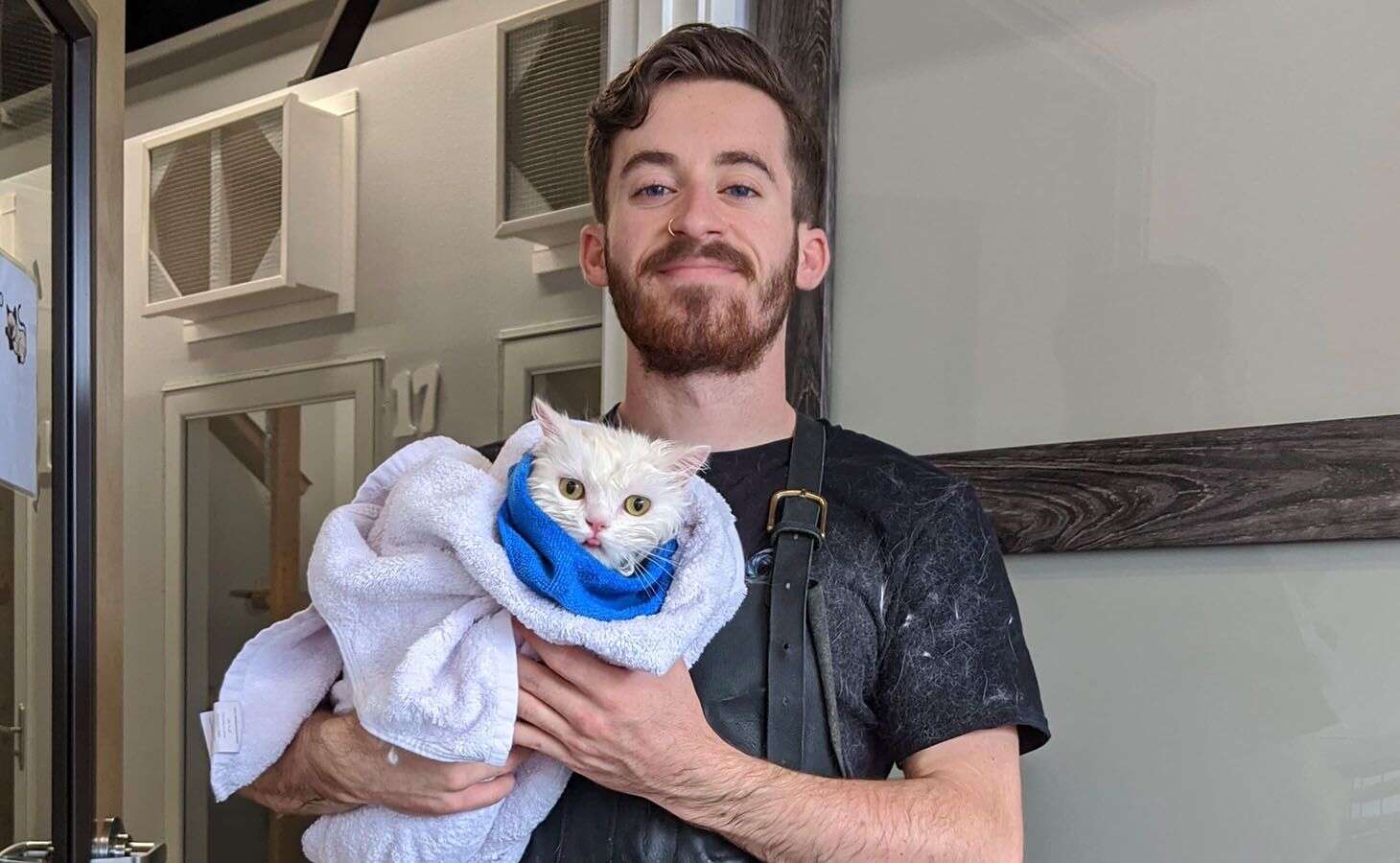 A smiling person holding a white cat wrapped in a blue towel.