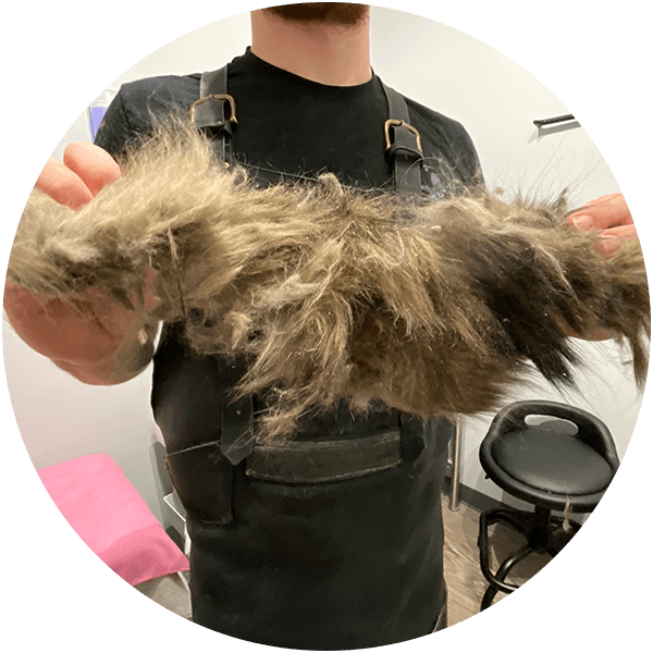 Person holding a clump of trimmed animal fur, wearing a black apron in a grooming salon.