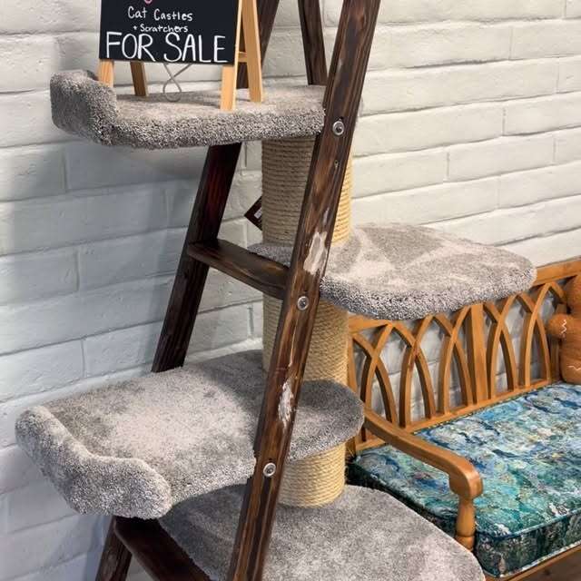 Wooden cat tower with carpeted platforms and a rope scratching post, next to a bench with a cushioned seat.